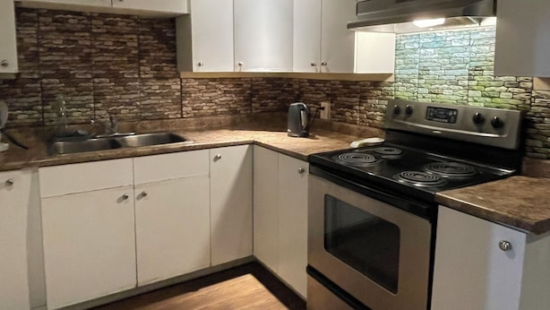 A modern kitchen with white cabinetry, a stone backsplash, and a stainless steel stove.