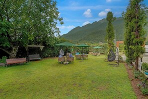 Uma área externa gramada com assentos, uma cadeira suspensa e vista para montanhas.