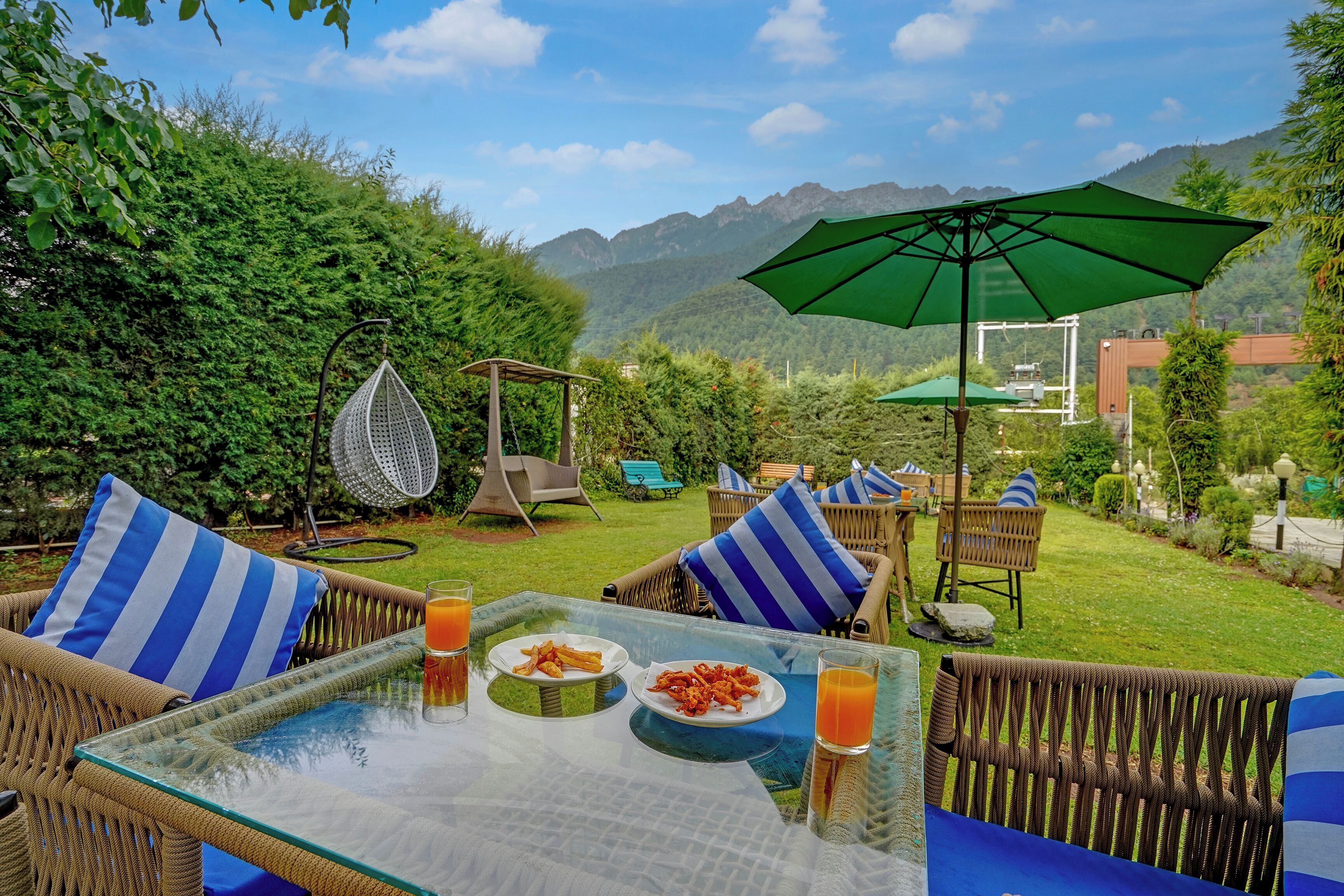 A dining area with wicker furniture, a glass table, and a view of mountains.