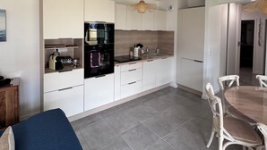 A modern kitchen with white cabinets, a built-in oven, and a dining area with a wooden table and chairs. - Stella Maris, the luxury apartment (Saint-Pierre-d'Oléron)