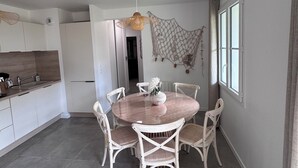 A modern kitchen with white cabinets, a round dining table with white chairs, and a hanging light fixture. - Stella Maris, the luxury apartment (Saint-Pierre-d'Oléron)