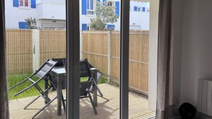 A room with a bed, a sliding glass door leading to an outdoor patio with a table and chairs, and a view of a residential area. - Stella Maris, the luxury apartment (Saint-Pierre-d'Oléron)