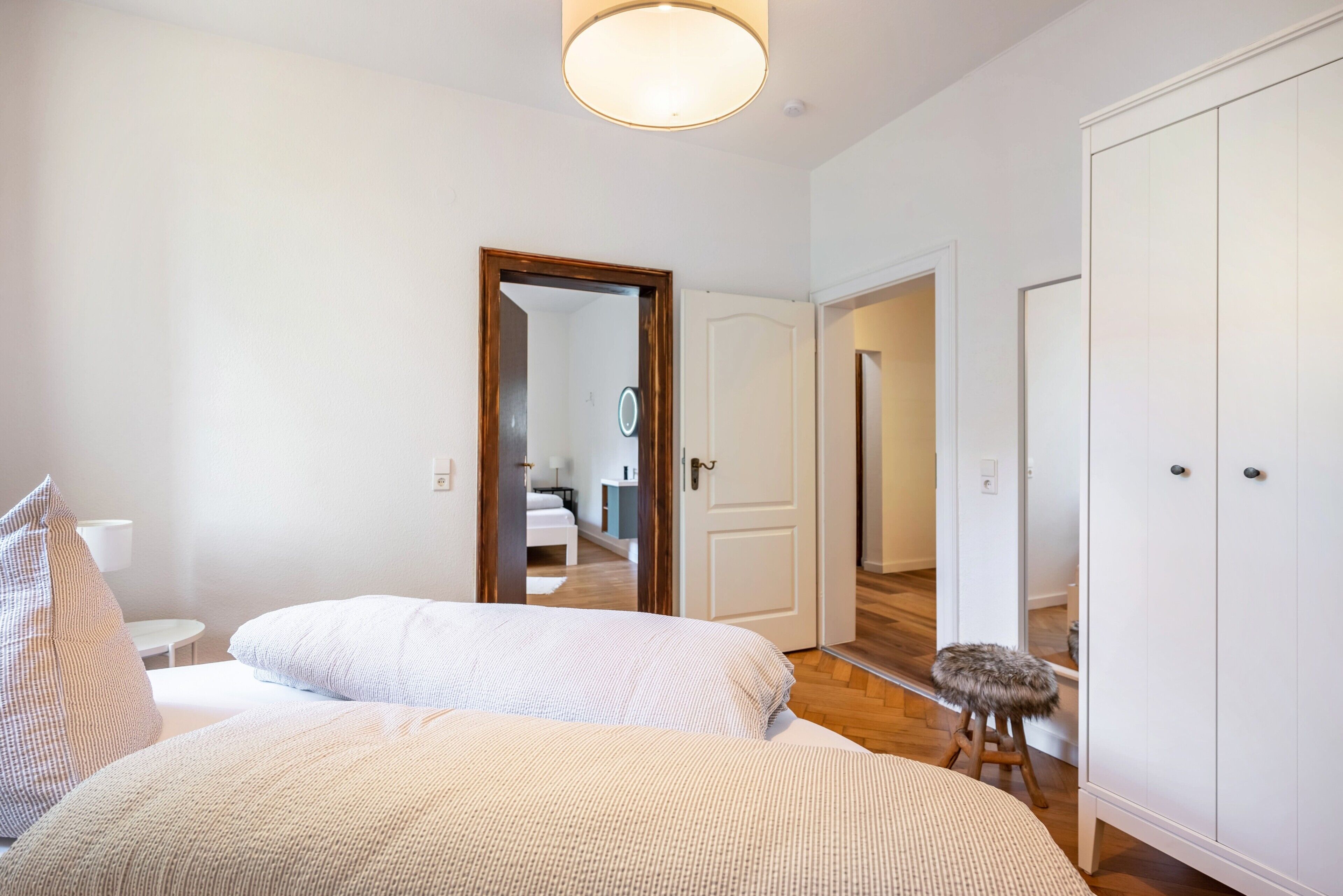 Ein Schlafzimmer mit zwei Betten, einem kleinen Hocker und einem Kleiderschrank.
