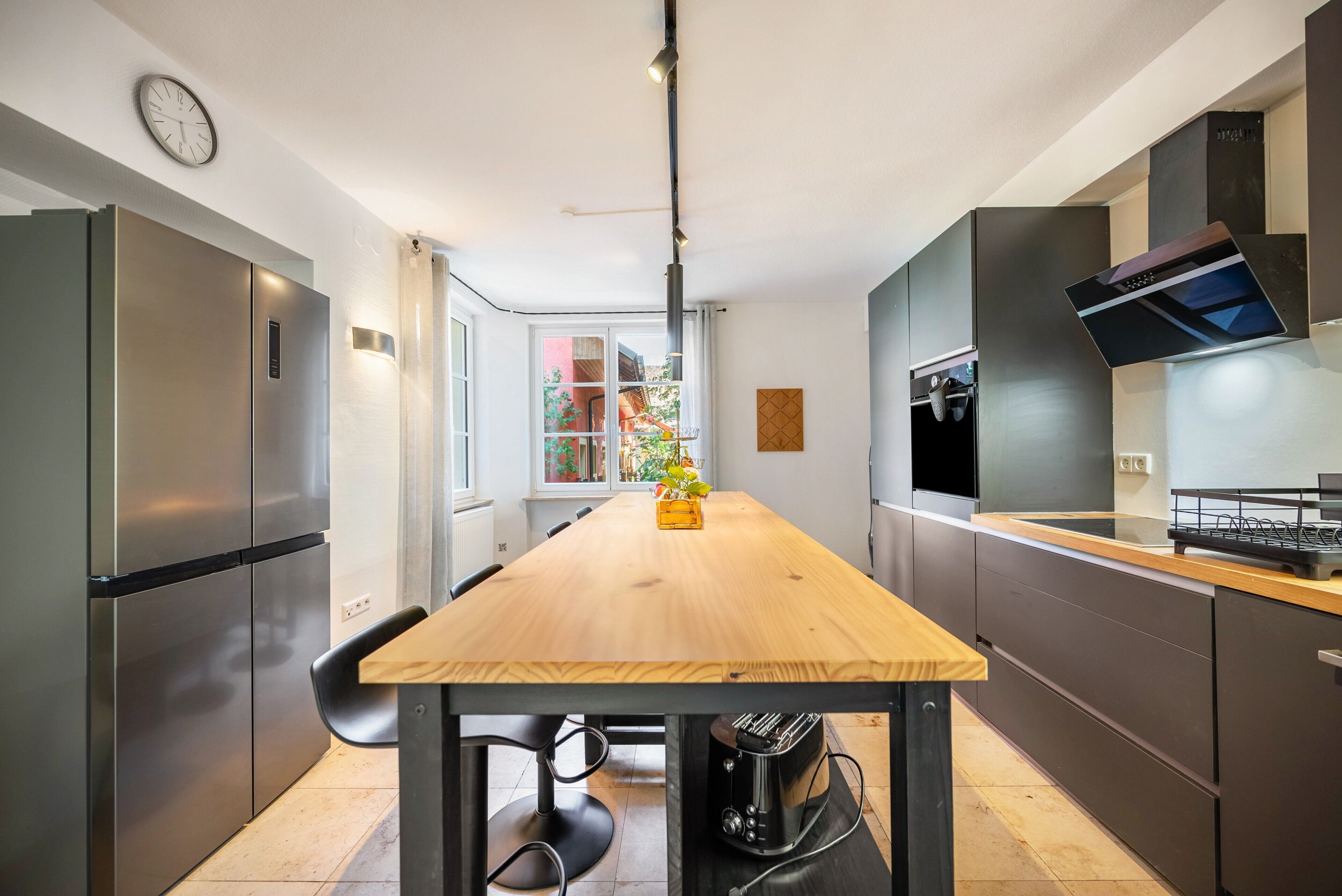 Eine moderne Küche mit Edelstahlgeräten, einem Holztisch und Blick auf einen Garten durch das Fenster.
