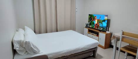Un dormitorio con cama, televisor, escritorio y silla.