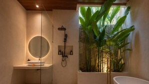 A modern bathroom with a round mirror, a freestanding bathtub, and a large window with plants. - Dangin Tukad Villa (Badung)