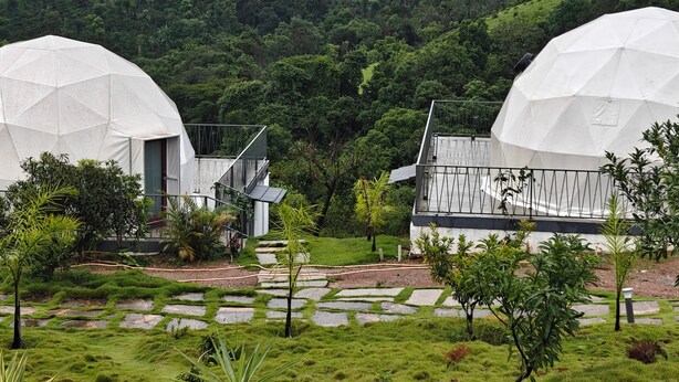 Two dome-shaped structures with a garden pathway leading to them, surrounded by lush greenery and hills. - The Divine Valley By Devandhari (Sakleshpur)