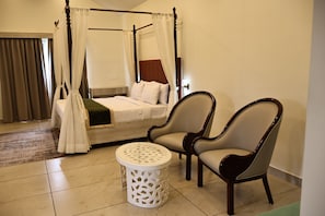 A four-poster bed with white linens, two upholstered chairs, a small round table, and a patterned rug. - The Divine Valley By Devandhari (Sakleshpur)