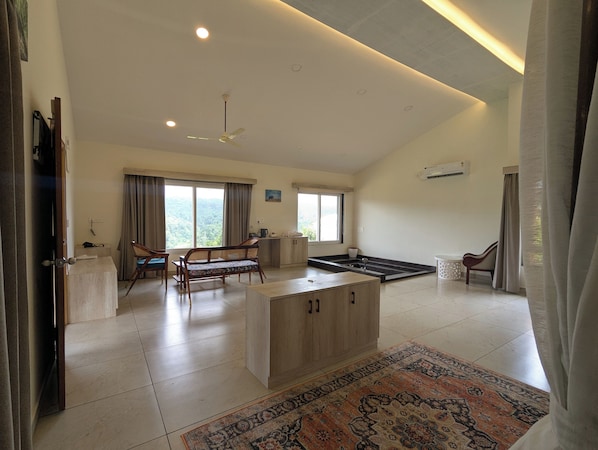 A spacious living area with a sofa, a coffee table, a ceiling fan, and a large window providing a view of the outdoors. - The Divine Valley By Devandhari (Sakleshpur)