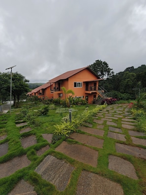 A two-story building with a red-tiled roof, surrounded by lush greenery and a stone pathway. - The Divine Valley By Devandhari (Sakleshpur)