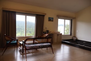 A room with two large windows, a wooden table, two wicker chairs, a small cabinet, and a sink. - The Divine Valley By Devandhari (Sakleshpur)