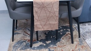 Ein Esstisch mit einem geometrisch gemusterten Tischläufer, zwei gepolsterten Stühlen und einer Vase mit weißen Blumen.