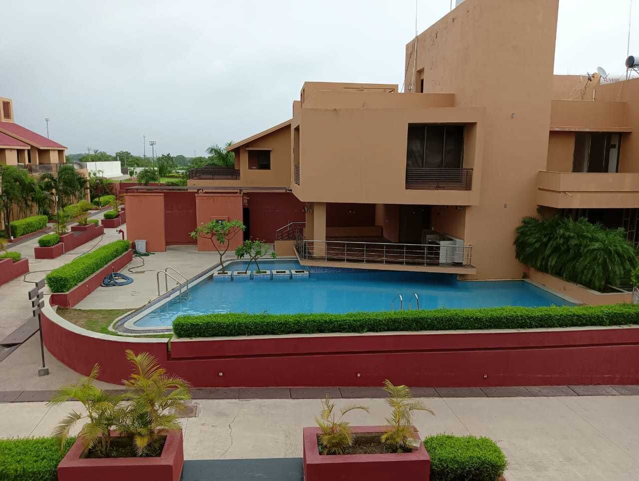 A swimming pool surrounded by a red wall and greenery, with buildings in the background.