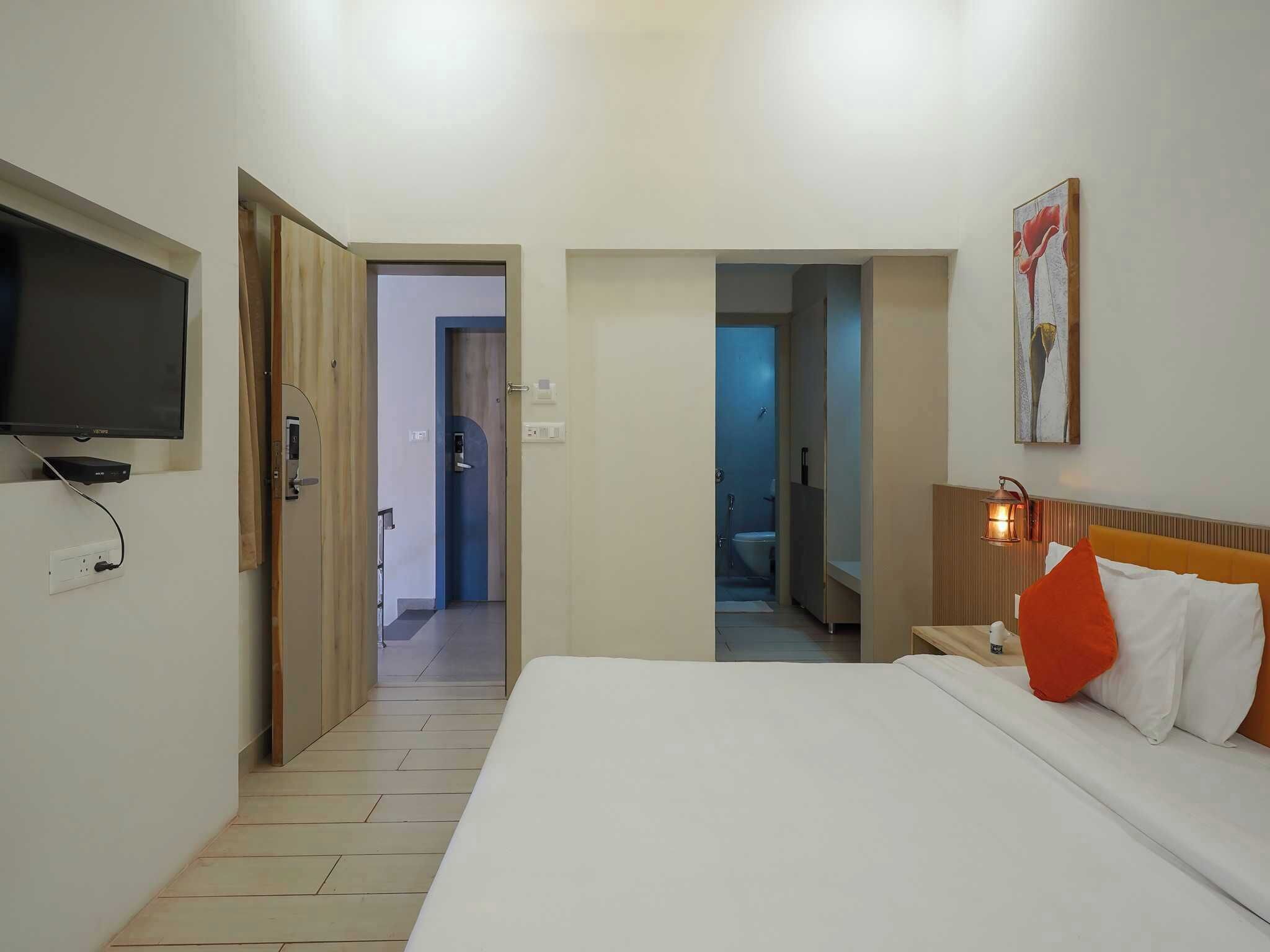 A hotel room with a bed, a television, a painting, and a bathroom visible through an open door.