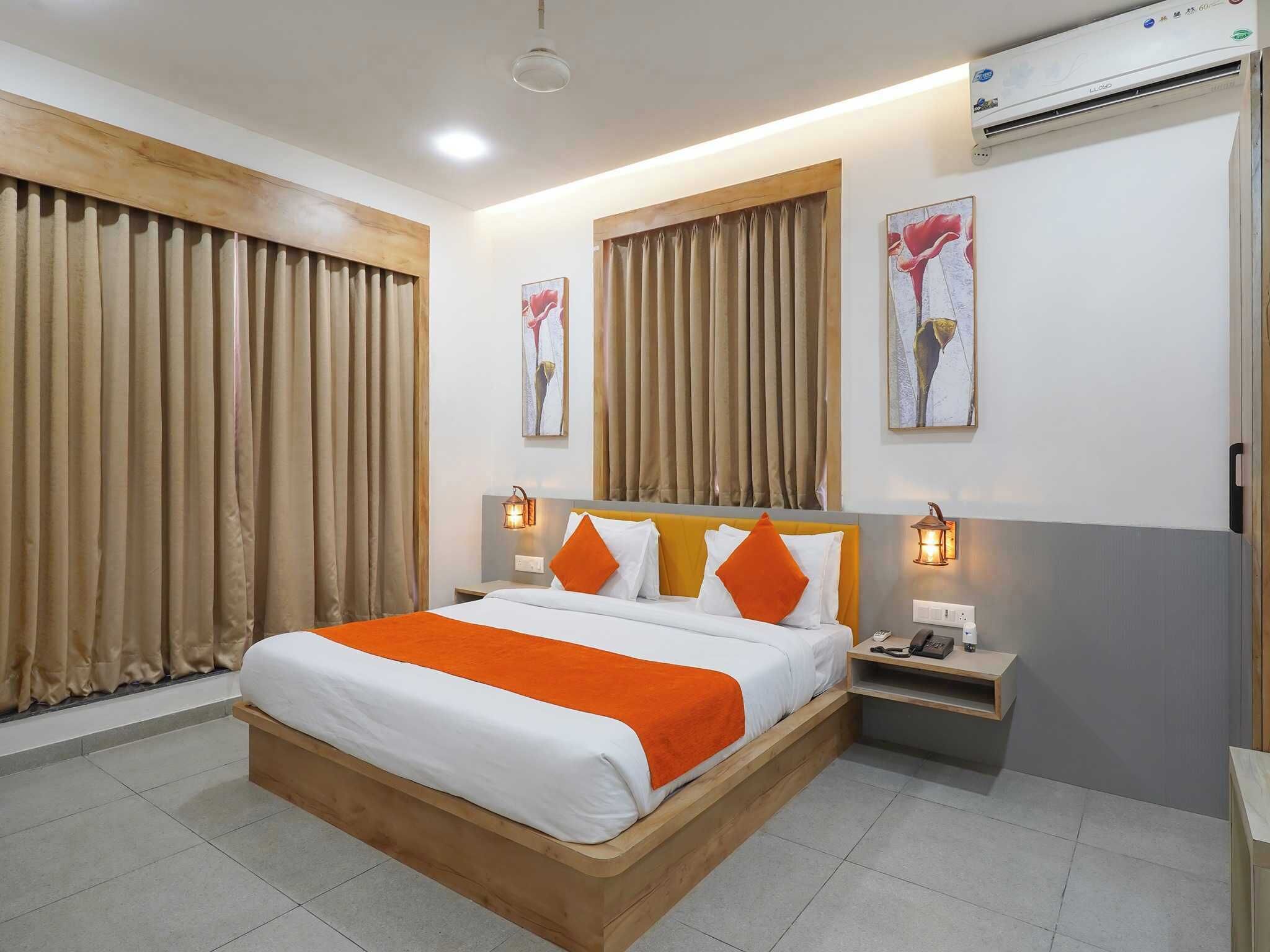 Habitación de hotel con cama de madera, cortinas color beige, una mesita de noche con lámpara y obras de arte en las paredes.