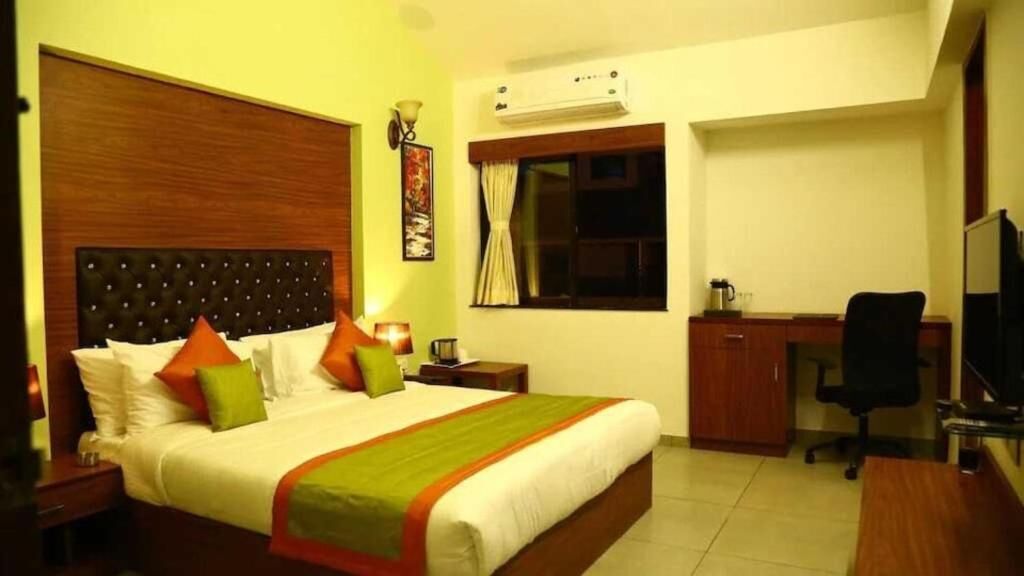 Habitación de hotel con cama, escritorio, silla, televisor, aire acondicionado y ventana con cortinas.