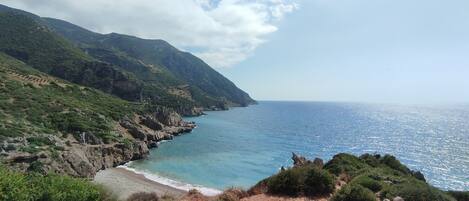 A coastal landscape with a rocky shoreline, green hills, and a clear sky.