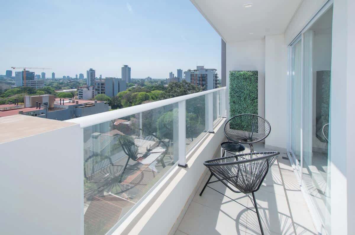 Un balcón con vistas despejadas de la ciudad, sillones modernos y barandilla de vidrio.