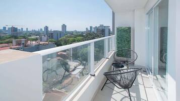Un balcón con vistas despejadas de la ciudad, sillones modernos y barandilla de vidrio.