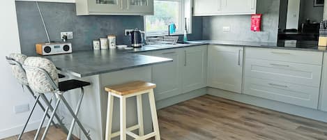 Una cocina moderna con una isla central, armarios blancos, una radio integrada y un taburete de madera.
