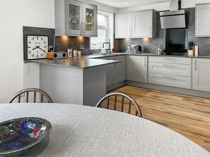 A modern kitchen with white cabinetry, a built-in oven, and a coffee machine.