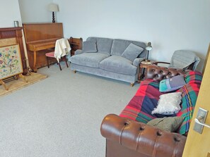A living room with a grey sofa, a brown leather armchair, a wooden piano, and a small table with a lamp.