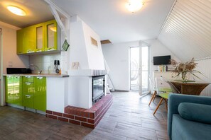 A modern kitchen with green cabinets, a brick fireplace, and a dining area with a clear chair and a blue sofa. - Holiday Home Right on the Lake, Terrace (Łobez)