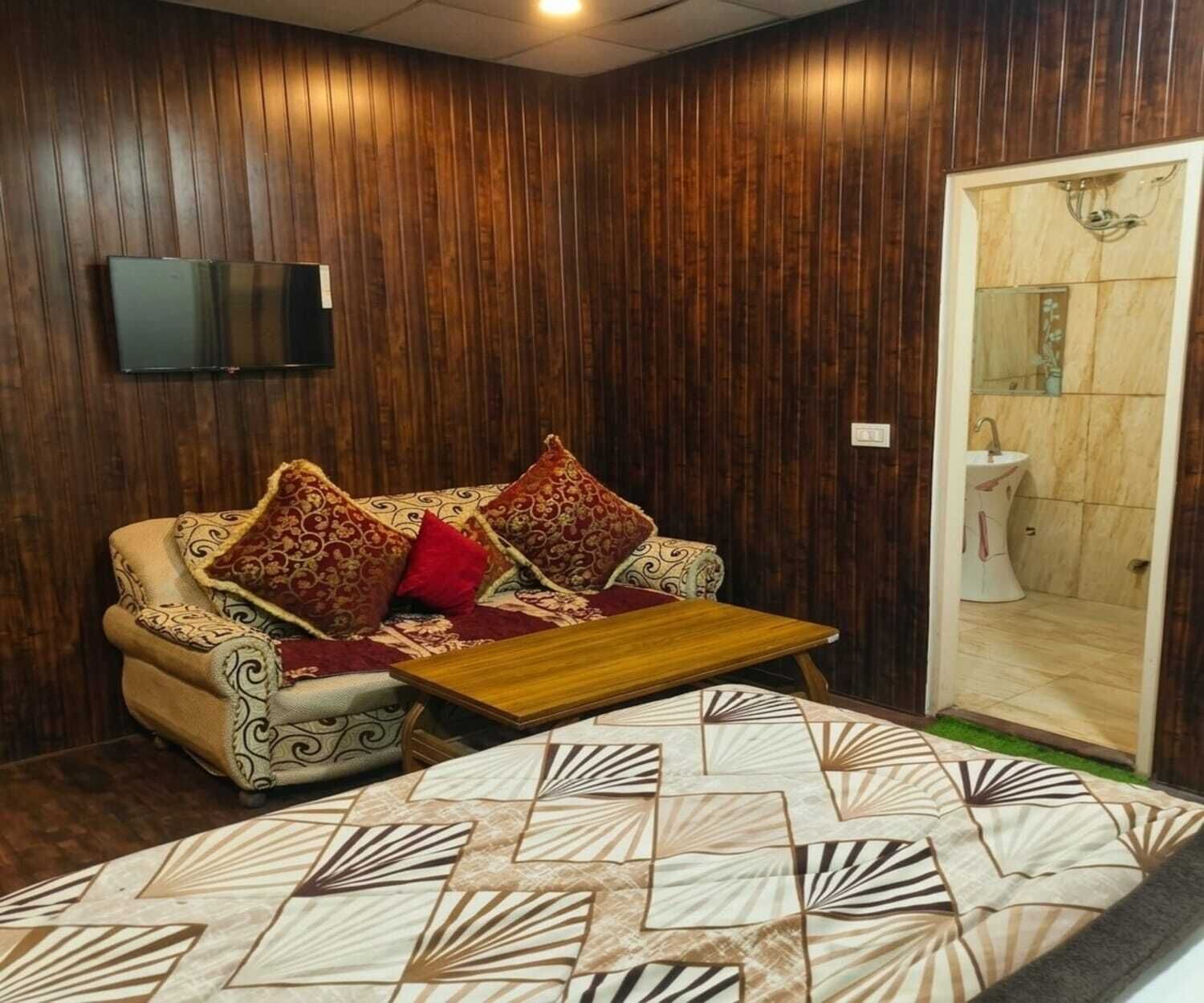 Una habitación con un revestimiento de madera, un sofá con cojines estampados, una mesa de centro y un baño visible a través de una puerta abierta.