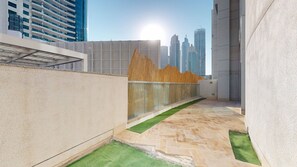 A rooftop terrace with a view of a city skyline, a geometric wall structure, and a small patch of artificial grass. - Aesthetic Four-Level 4 Bedroom l near Marina Walk (Dubai Marina)