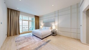 A modern hotel room with a large bed, a nightstand, a window with curtains, and a view of the city. - Aesthetic Four-Level 4 Bedroom l near Marina Walk (Dubai Marina)