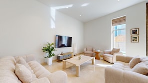 A modern living room with a flat-screen TV, beige sofas, a coffee table, and a potted plant. - Aesthetic Four-Level 4 Bedroom l near Marina Walk (Dubai Marina)