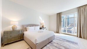 A hotel room with a large bed, two bedside tables with lamps, a view of the city through large windows, and a cityscape visible outside. - Aesthetic Four-Level 4 Bedroom l near Marina Walk (Dubai Marina)