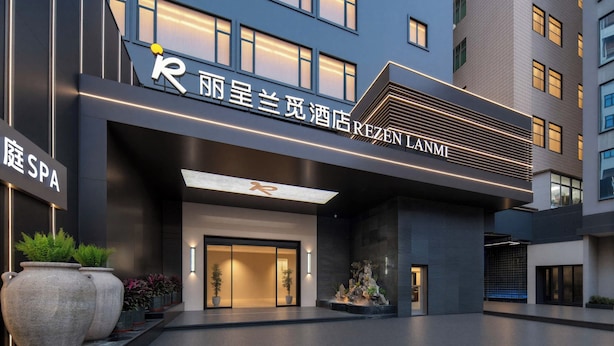 L’entrée d’un hôtel, avec une façade moderne, de grands pots de plantes et un panneau indiquant la présence d’un spa.