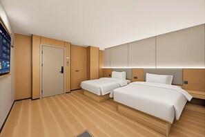 Une chambre d’hôtel avec deux lits, un plancher en bois, une porte et un téléviseur fixé au mur.