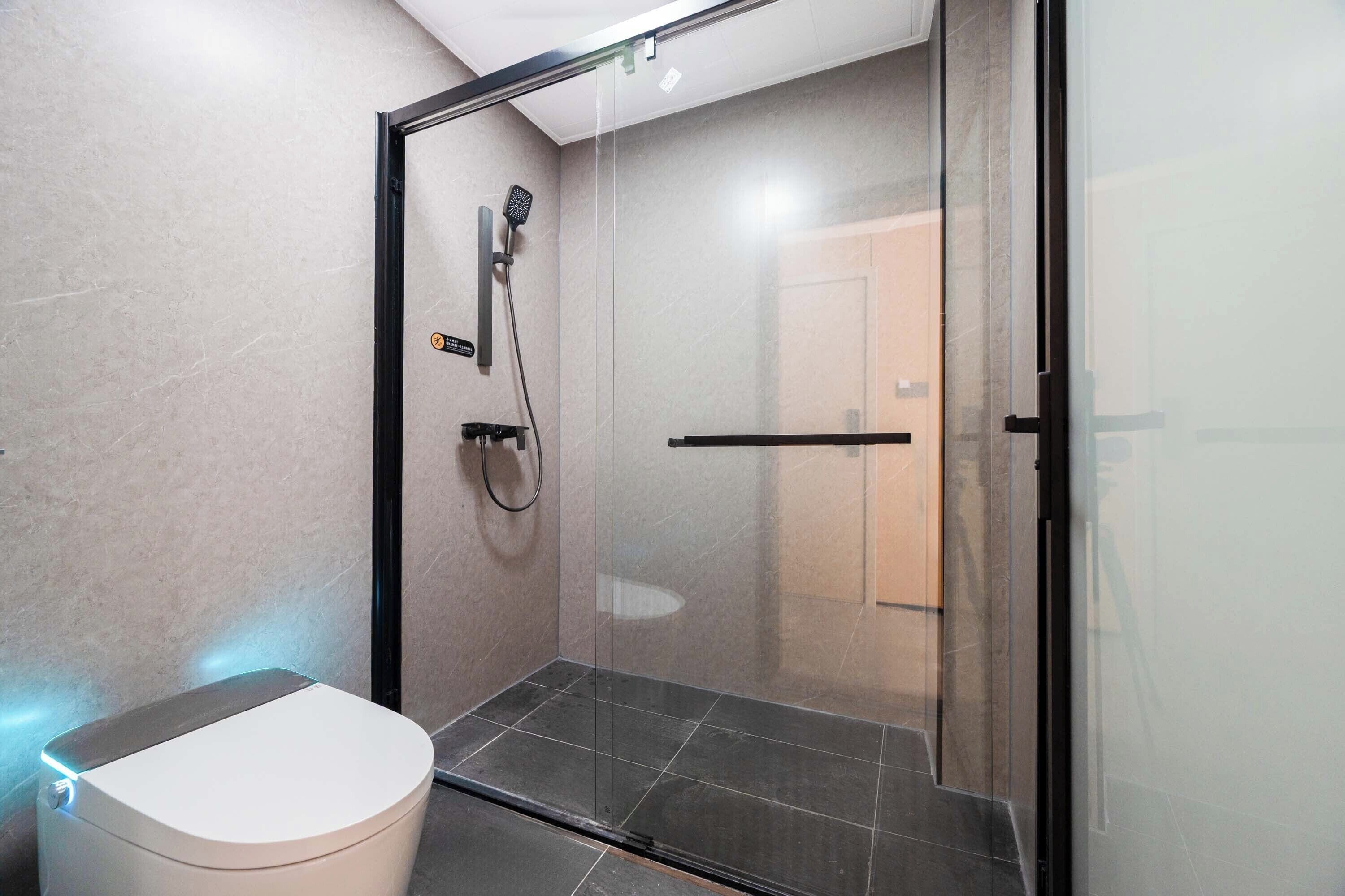Ein modernes Badezimmer mit einer gläsernen Duschkabine, einer weißen Toilette und einem Fliesenboden.