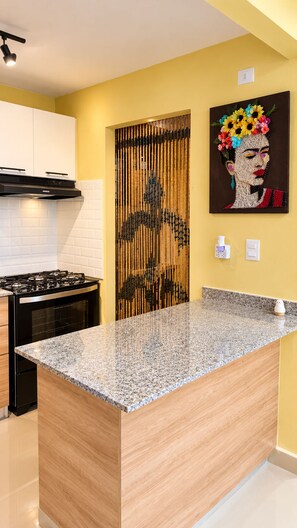 A kitchen with a granite countertop, a stove, and a wall-mounted artwork. - Modern 3BR Apartment Near SDQ Airport with Free Parking, Fast Wi-Fi (Santo Domingo Este)