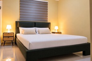 A modern bedroom with a large bed, two bedside tables with lamps, a dark headboard, and a window with blinds. - Modern 3BR Apartment Near SDQ Airport with Free Parking, Fast Wi-Fi (Santo Domingo Este)