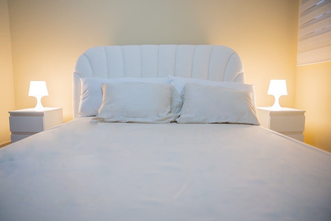 A bed with white bedding and pillows, flanked by two bedside tables with lamps, in a room with a plain wall and a slanted ceiling.