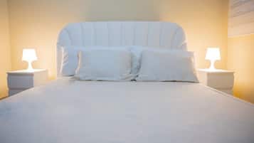 Un lit avec une literie et des oreillers blancs, flanqué de deux tables de chevet avec des lampes, dans une pièce dont le mur est uni et le plafond est en pente.