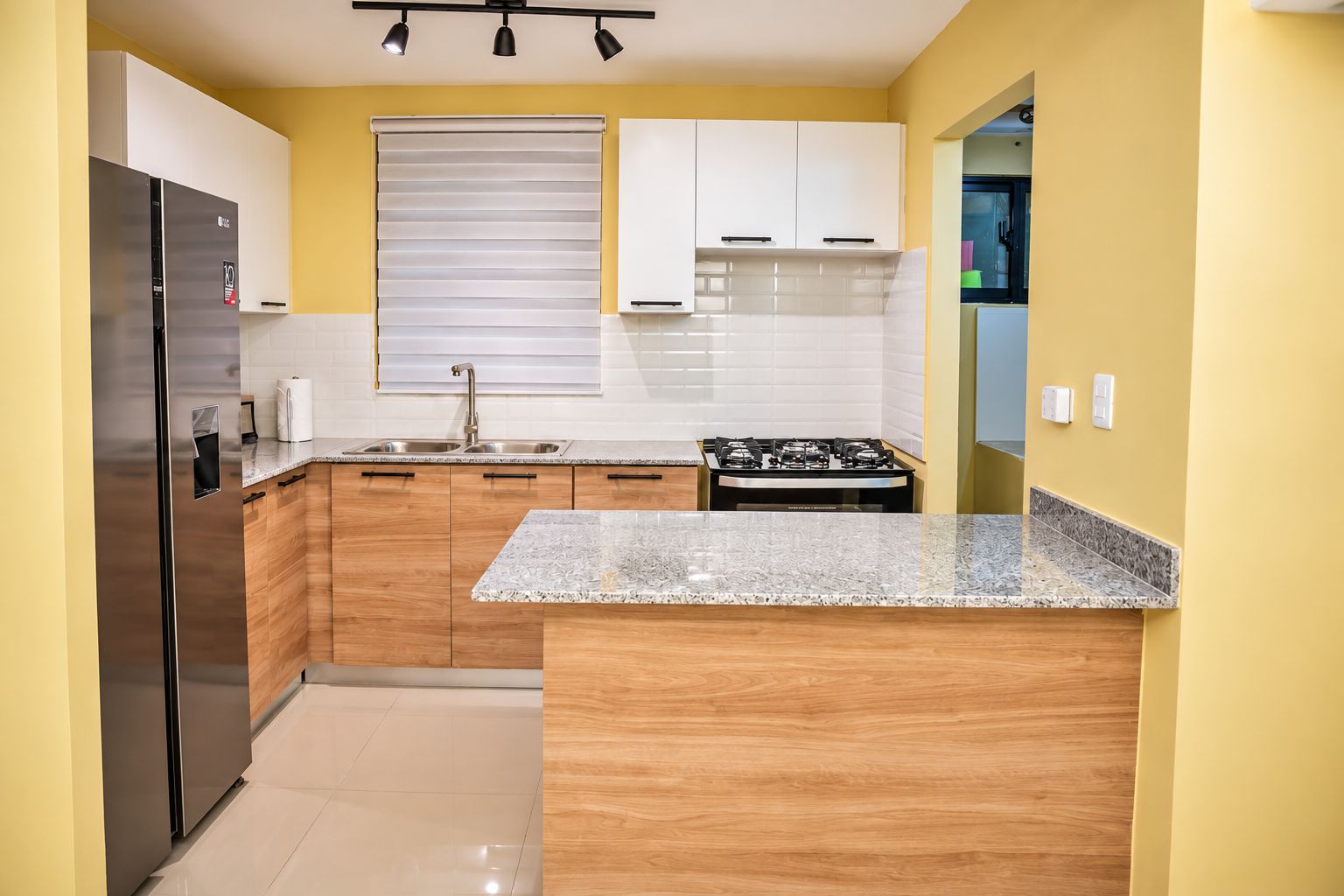 A modern kitchen with wooden cabinets, a stainless steel refrigerator, a gas stove, and a granite countertop.