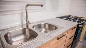 Una cocina con un lavamanos de acero inoxidable doble, estufa a gas y armarios de madera.