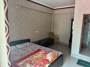 Una habitació petita i senzilla amb un llit, un escriptori i una cadira. Hi ha una porta que dona a un bany.