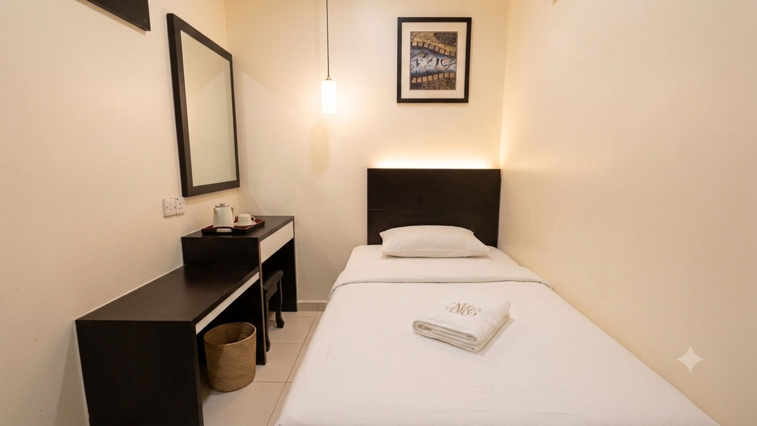 Quarto de hotel pequeno e bem arrumado, com uma cama de solteiro, mesa de cabeceira, espelho e luminária fixada na parede.