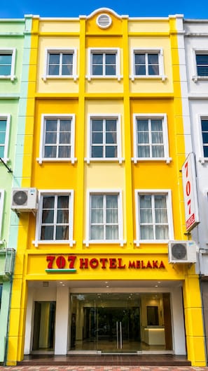 Un hotel con una fachada amarillo brillante, numerosas ventanas y un cartel que indica que es el Hotel Melaka 707.
