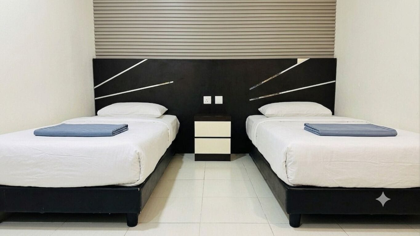 A room with two beds, a nightstand, and a wall-mounted light fixture.