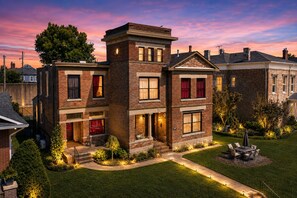 A multi-story residential building with a brick facade, large windows, and a well-maintained lawn.