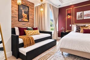 A modern bedroom with a sofa bed, a separate bed, a brick wall, a picture of a deer, and a cityscape on the wall.
