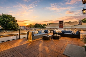 Une terrasse sur le toit avec des sièges extérieurs, une vue sur le coucher de soleil et un panorama de la ville en arrière-plan.