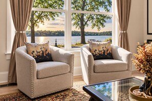 Una habitación con dos sillones mirando hacia un ventanal con vistas a un lago y árboles.