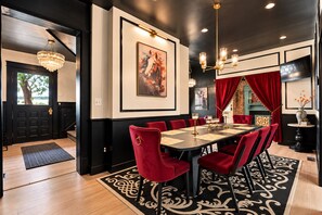 A dining area with a long table, red upholstered chairs, and a chandelier.